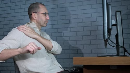 Man Stretches at Computer Desk in Office Setting