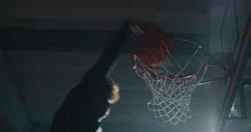 Cinematic slow motion shot of an young professional male player is making a slam dunk during a bas