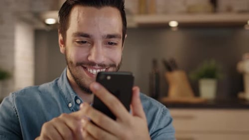 Man Smiling Using Smartphone at Home in Kitchen