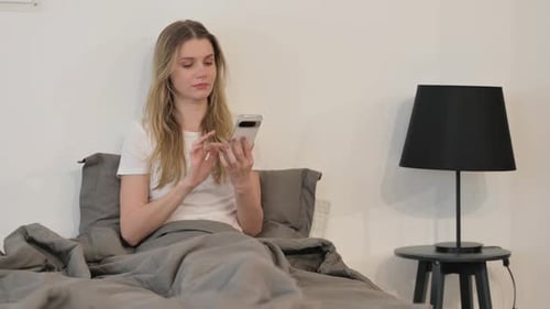 Woman Using Phone Sitting in Bed Indoors