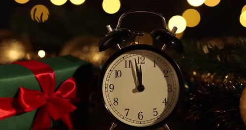 New Year celebration. Alarm clock and festive decor on table against blurred lights, closeup