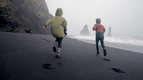 man and woman running on reynisfjara black sand beach in iceland