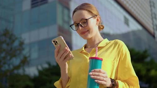 Happy caucasian girl manager young business woman standing in city street looking into mobile phone