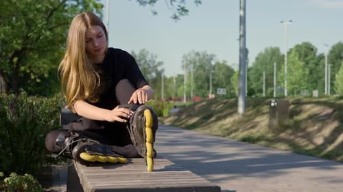 young beautiful girl in park tying laces on roller skates before skating workout active lifestyle