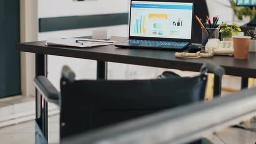 Wheelchair in Office and Laptop on Desk Showing Business Analytics