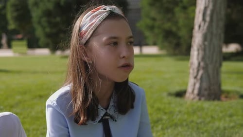 Closeup of a Girl Eating an Apple in the Schoolyard Sitting on the Green Grass
