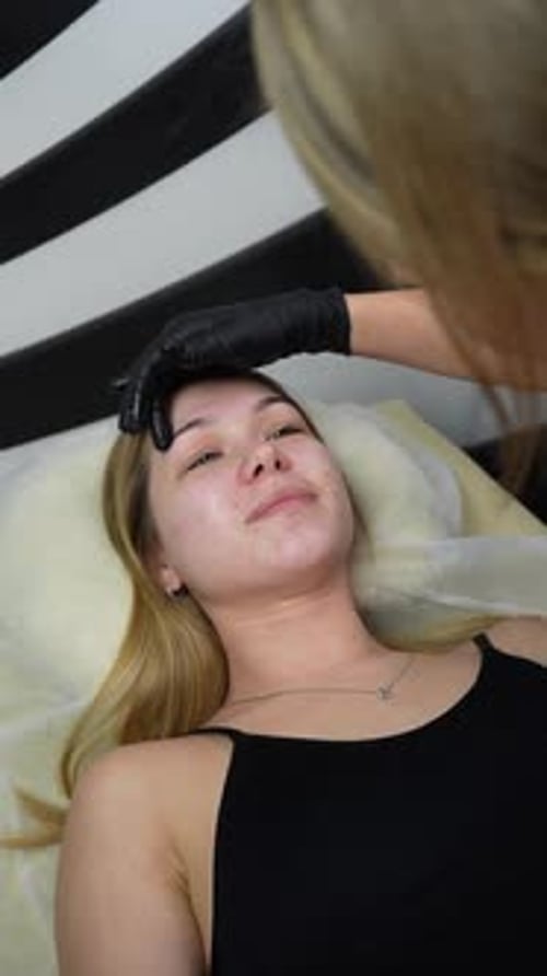 Hair removal master applies wax on client's face. Eyebrow correction with wax. Close up