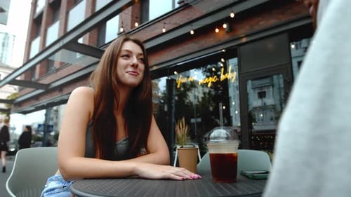 Attractive young couple having lunch sitting at cafe table outdoors, drinking coffee and talking.