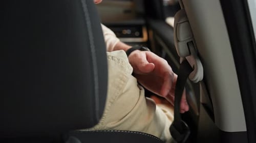 View From Backseat to Unrecognizable Man Sitting on Front Passenger Seat Fastening Belt Harness