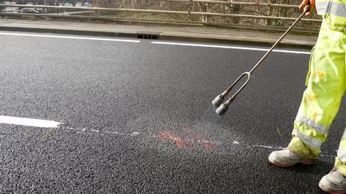 Contractor with propane gas flame torch melting tarmac road asphalt marking paint