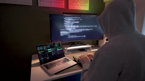 Un hacker cagoulé codant sur un ordinateur portable et un écran, vue latérale