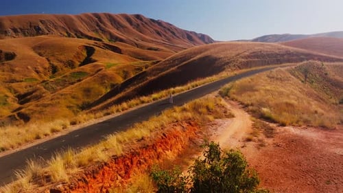 Young Girl Walks Along a Paved Road That Turns Into a Dirt Path Surrounded By the Red Hills of the