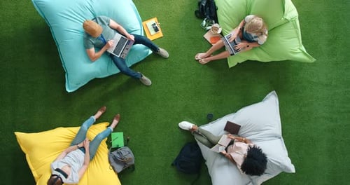 Students using modern technology and sitting on bean bag in a library from above