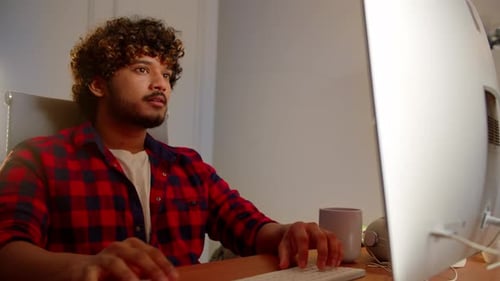 Ein Mann mit lockigem Haar und Bart schaut sich etwas auf dem Monitor an und tippt auf der Tastatur A