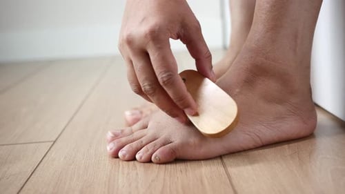 Using a Brush the Person Gently Brushes Their Foot on the Hardwood Flooring