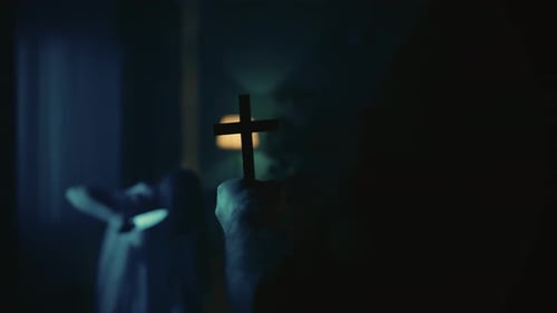 Man Holds Cross in Dark Room