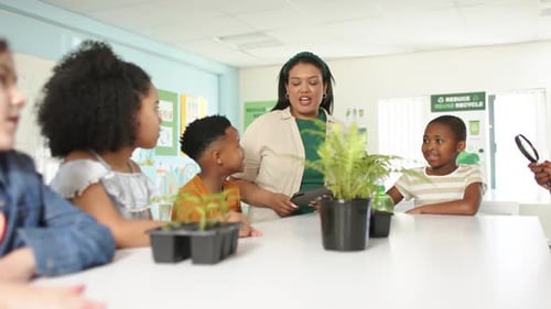 African American teacher greeting and guiding children observing plants with tablet, lens in class