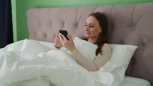 Woman Using Smartphone in Bed at Home