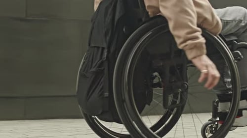 Man with Disability Riding Wheelchair along Sidewalk in City