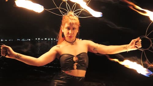 A young woman dancing with her fire ring at night during her show in front of the pier