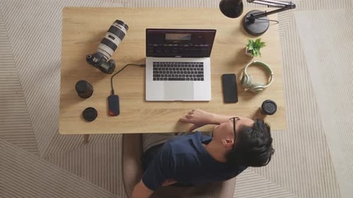 Vista superior de un hombre asiático que gradúa el color con dolor de espalda mientras usa una computadora portátil editando el Vídeo