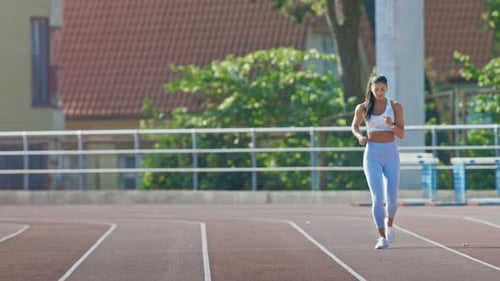 Beautiful Fitness Woman in Light Blue Athletic Top and Leggings Jogging in a Stadium. She is Runnin