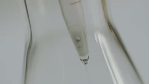 Close Up of Liquid Falling from Test Tube into Flask in Scientific Laboratory.
