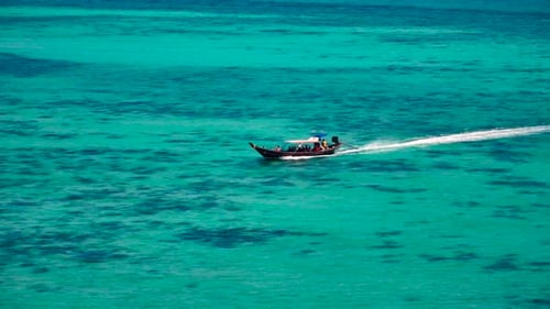 Drone shot of a small boat sailing next to the island.