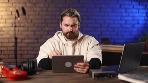 Musician Using Tablet at Laptop at Dark Recording Studio