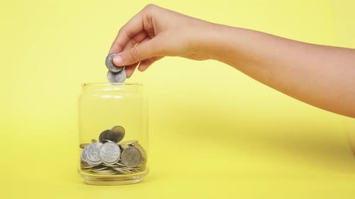 Hand Adding Coins to Glass Savings Jar