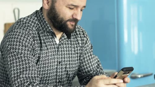 Man using a phone sitting at kitchen table