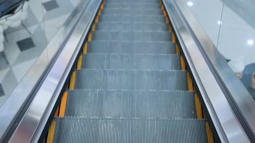 Ascending Escalator with Glass Frame and Reflections in Modern Shopping Mall