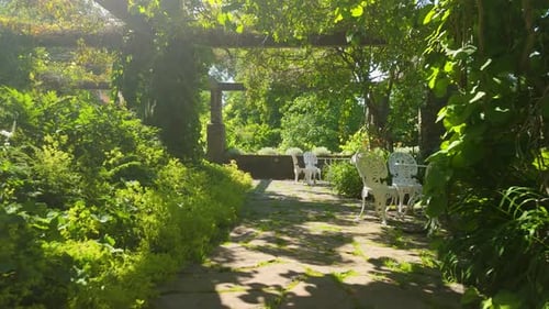 Push in shot of garden pergola with white outdoor furniture and stone paving at Baldersnas Manor
