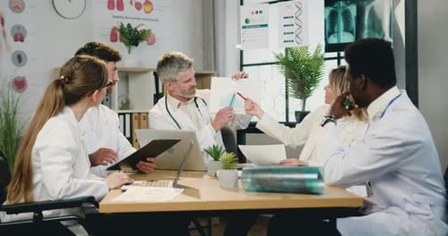 Multicultural man and woman doctors discussing report with charts during joint meeting in clinic
