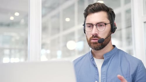 Confident businessman in a headset talking on a video call using a laptop at workplace in modern