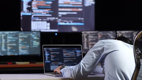 Vue arrière rapprochée d'un programmeur asiatique s'appuyant sur une table tout en écrivant du code par un ordinateur portable
