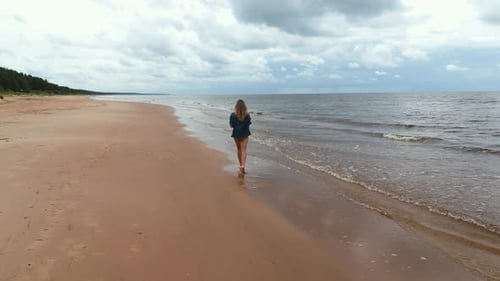 Beautiful Woman is Walking Along a Sandy Beach Near the Ocean