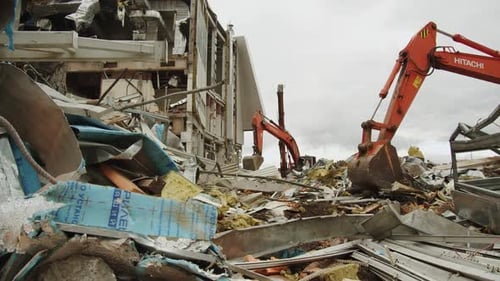 Excavators Dismantle Rubble Near Stadium Under Cloudy Sky