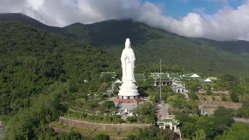 Aerial drone view of tall Lady Buddha statue and temples with huge mountains and ocean in Da Nang, V