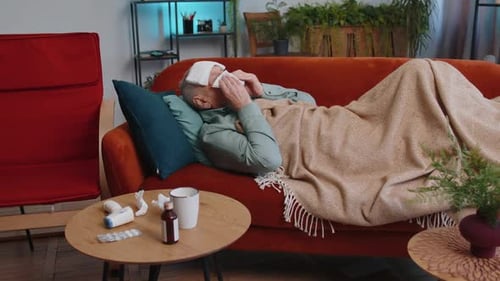 Un homme âgé malade souffrant d'une allergie au froid, allongé sur le canapé de la maison, éternue avec de la morve dans une serviette