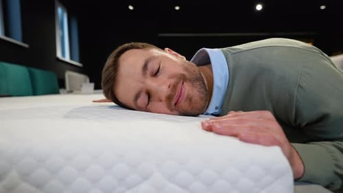 Young Handsome Man Examining Orthopedic Mattress at Furniture Store