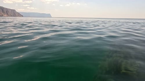 Sea Water Surface Camera Flies Over the Calm Azure Sea with Volcanic Rocky Shores on Background