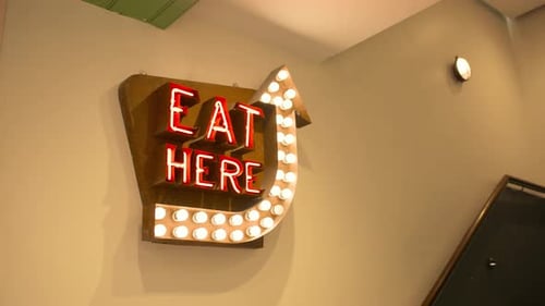 Slow motion of 'Eat Here' neon sign hanging in food court dining area