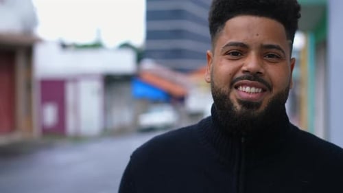 One happy young black Brazilian man walking in city street forward toward camera smiling. 20s South