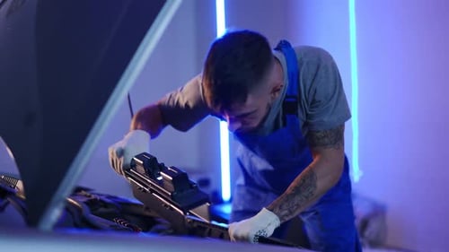 Junger konzentrierter Mann untersucht mit Taschenlampe einen Automotor in der Garage