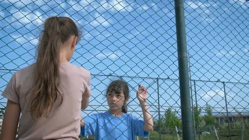 Two Children by Metal Fence on Sunny Day