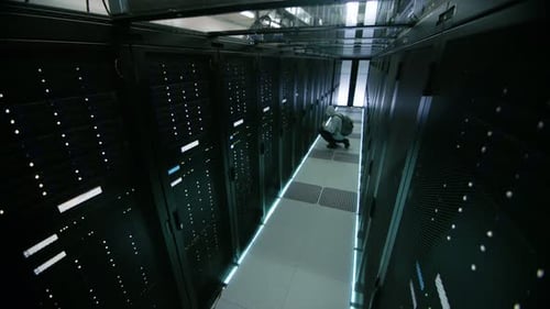 Security Camera Footage of a Hooded Hacker in Data Center, With His Laptop He Connects to One of Th