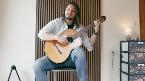 Man Playing Guitar and Singing Indoors on Stool