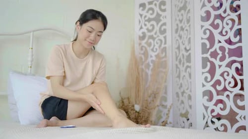 Woman Applying Lotion to Leg on Bed