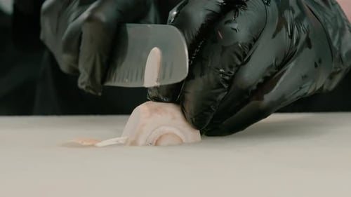 Close-up of a sushi maker in gloves cutting a mushroom on a white board in a professional kitchen
